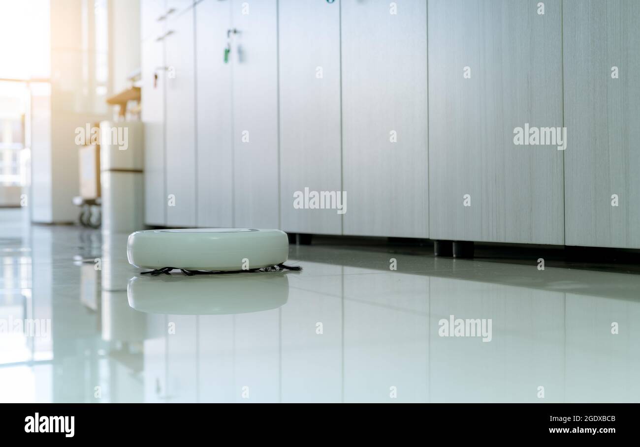Robot vacuum cleaner cleaning floor in office. White robot vacuum cleaner for the smart home concept. Cleaning robot for cleaning floor. Wireless Stock Photo