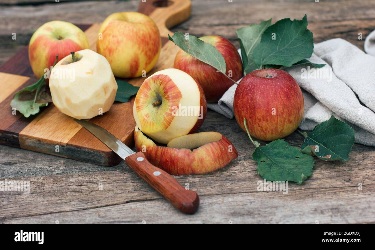 Apples, peeled from the peel, lie on a wooden board and a table. Harvest season, cooking at home, autumn food and holiday Stock Photo