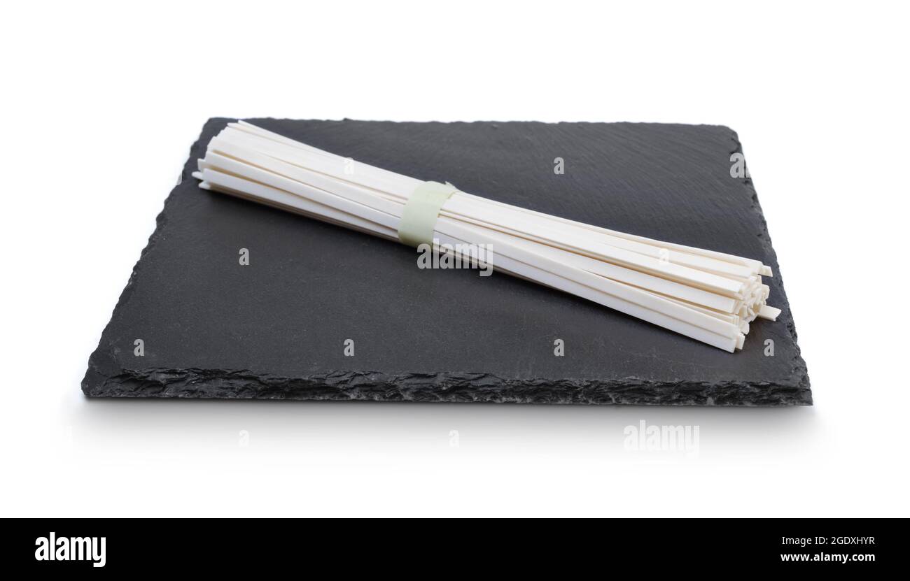 Raw rice noodles on black slate plate isolated on white. Stock Photo