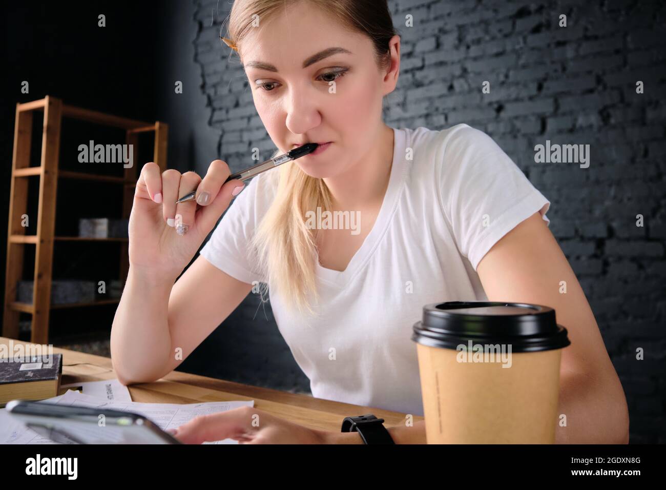 Pensive woman reads a message holding pen in mouth Stock Photo