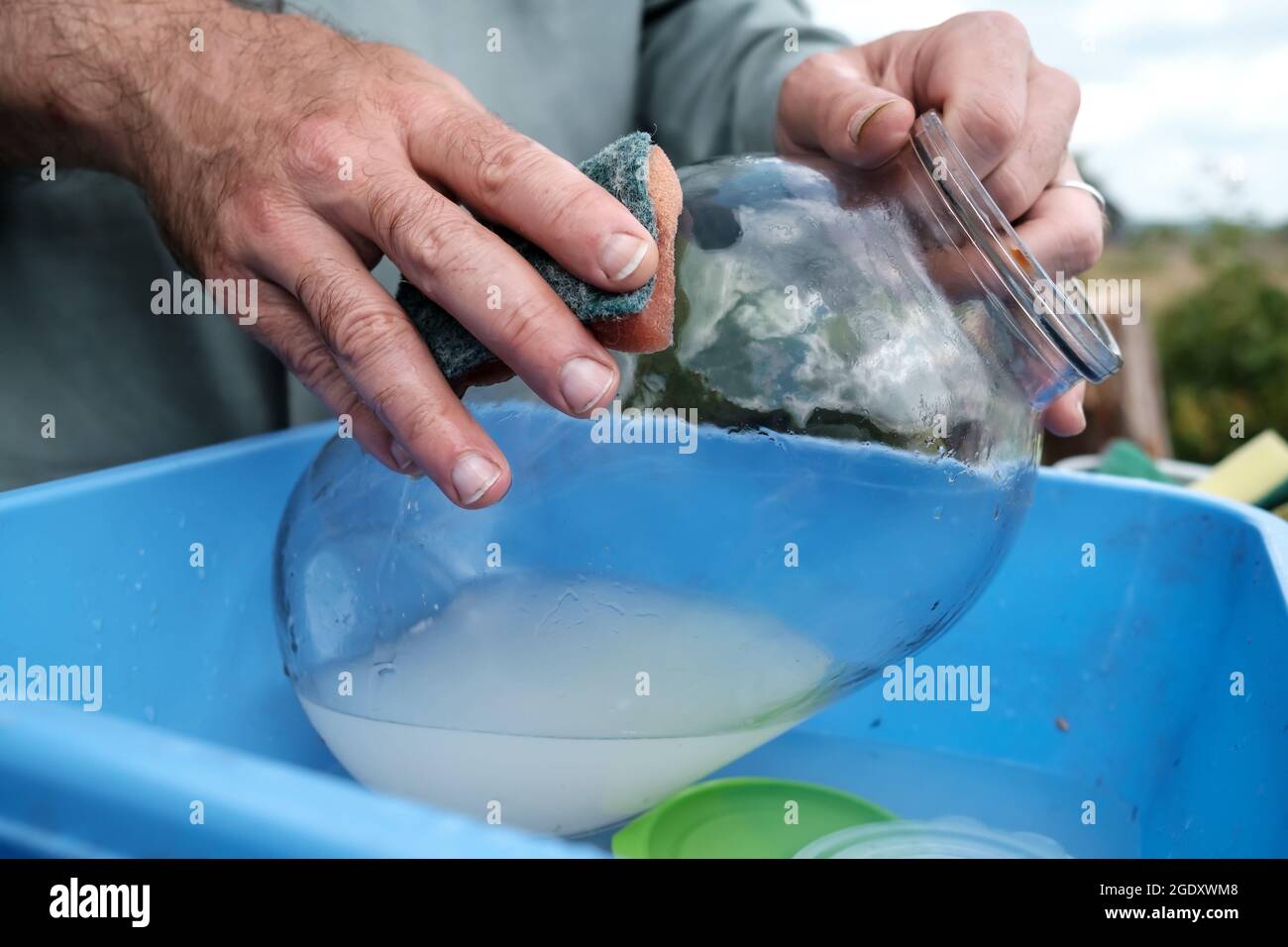 Male hands wash a dirty glass jar with a sponge, in a plastic basin, in