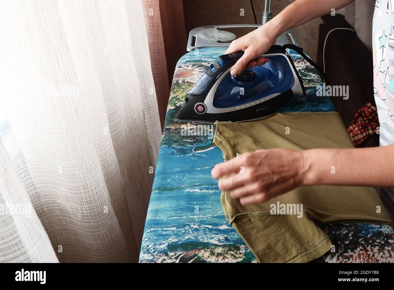 a woman irons children's clothes on an ironing board with an iron Stock