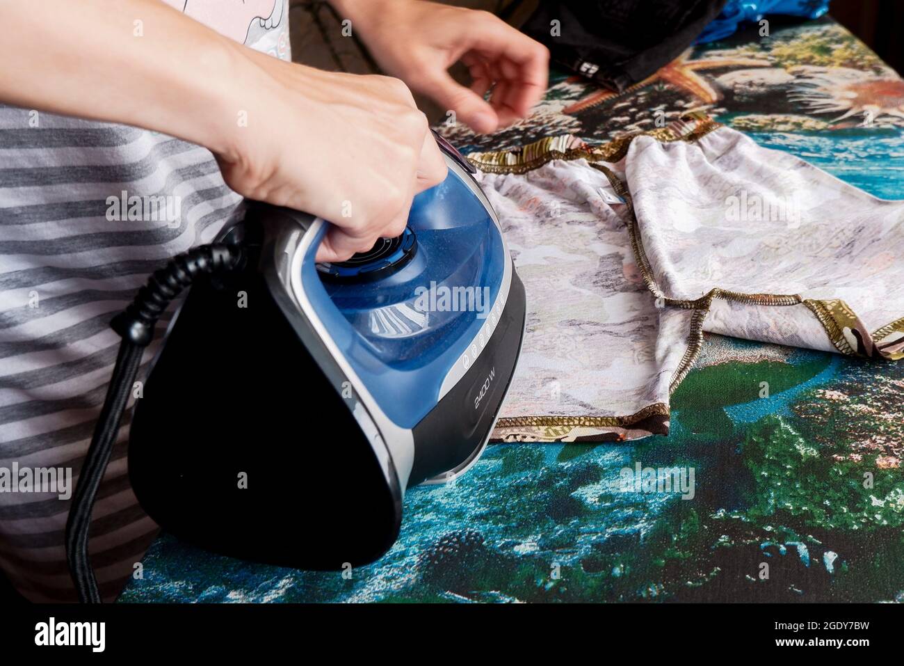 a woman irons children's clothes on an ironing board with an iron Stock