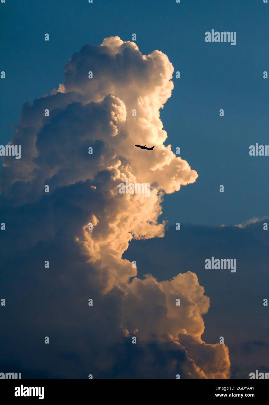 A commercial airliner passes by a large thunderhead cloud shortly after takeoff. Stock Photo