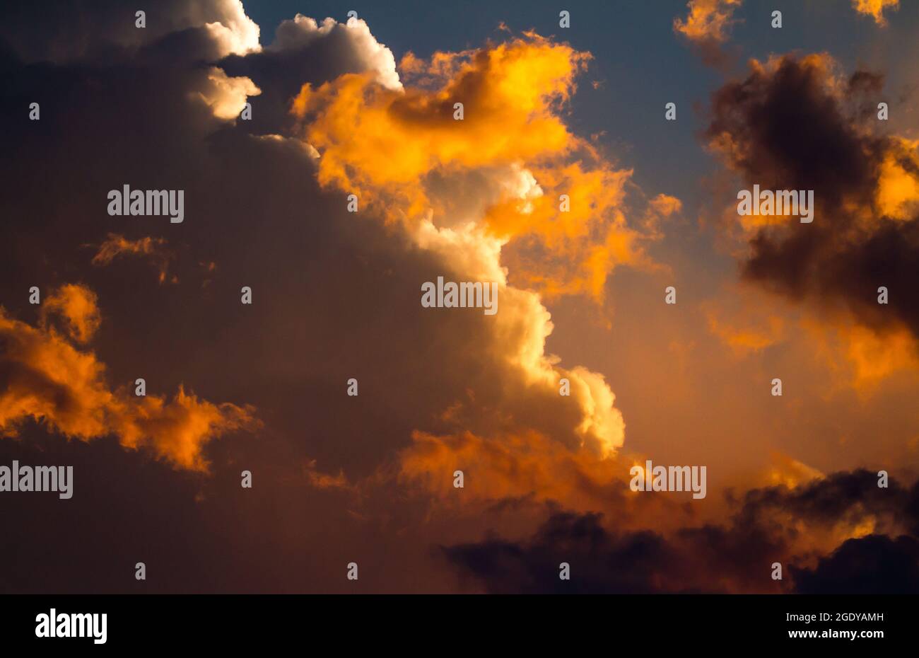 The setting sun bathes gathering storm clouds in a dramatic orange glow. Stock Photo