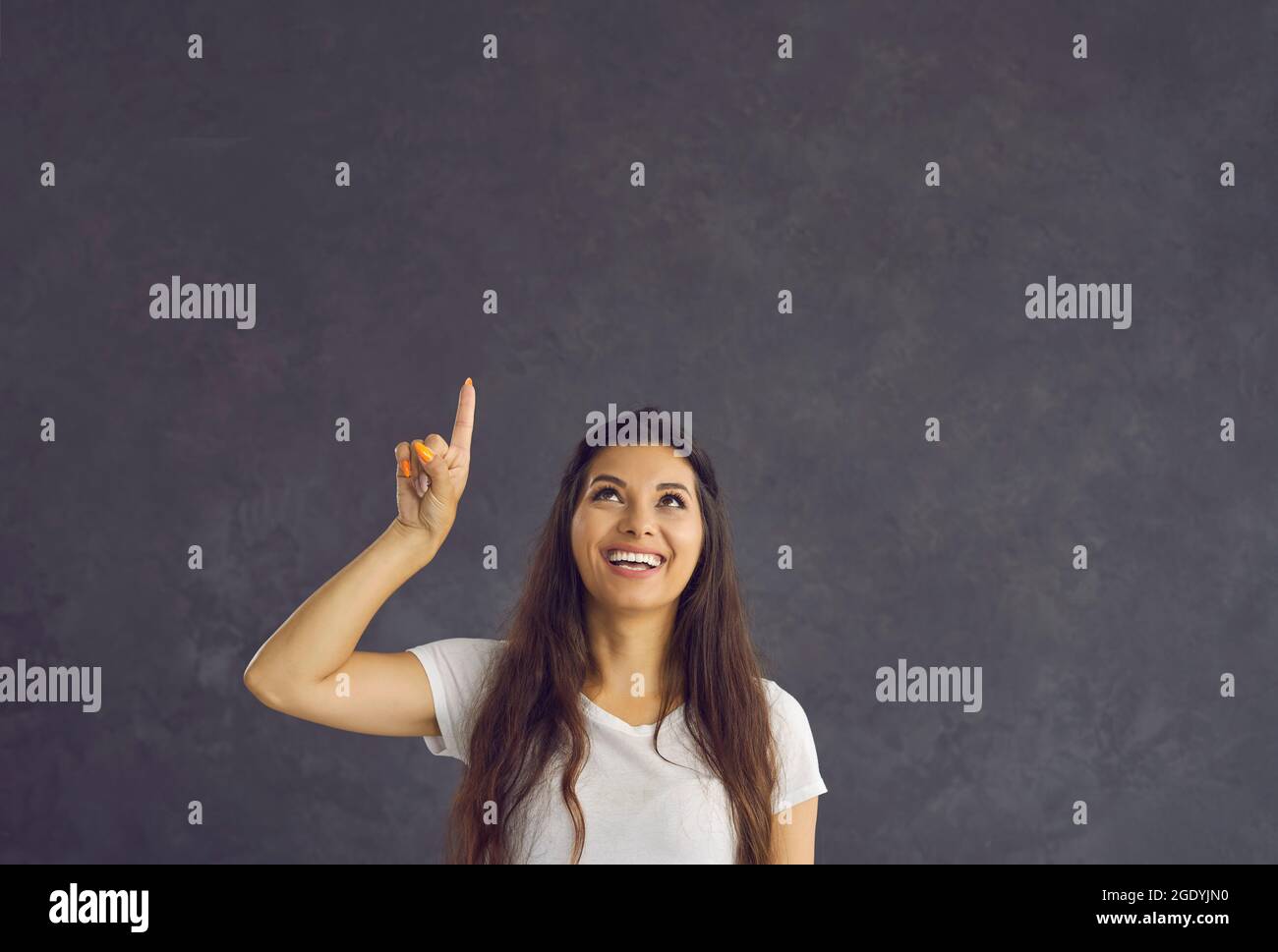 Happy young woman pointing index finger up at copy space recommending something. Stock Photo