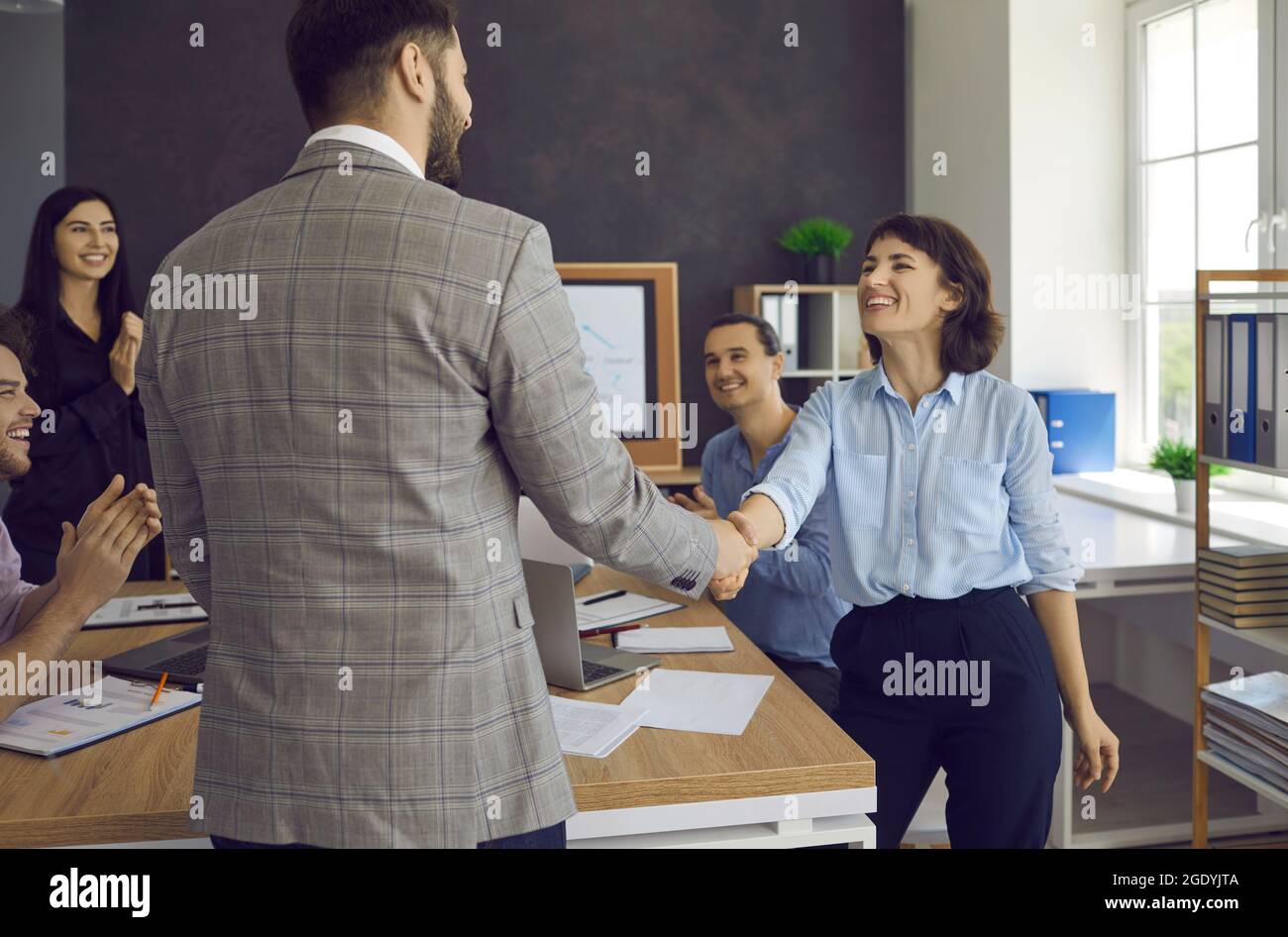 Two happy young people shaking hands in a business meeting with their colleagues Stock Photo