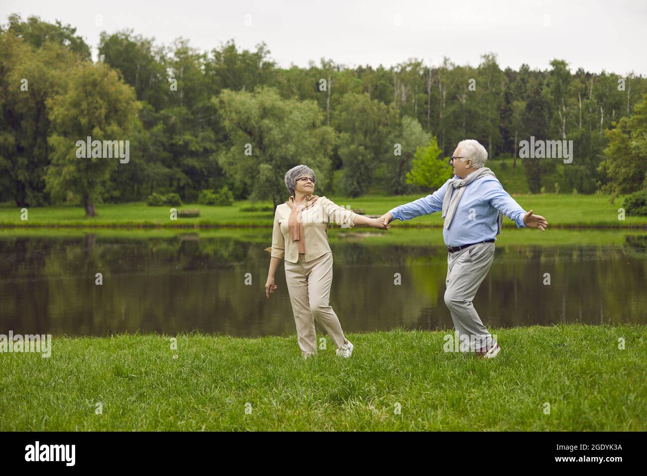 Happy senior couple taking a stroll by the river in a green park on a nice summer day Stock Photo