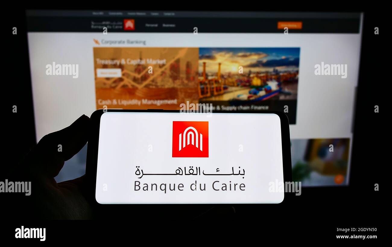Person holding smartphone with logo of Egyptian bank Banque du Caire on screen in front of website. Focus on phone display. Stock Photo