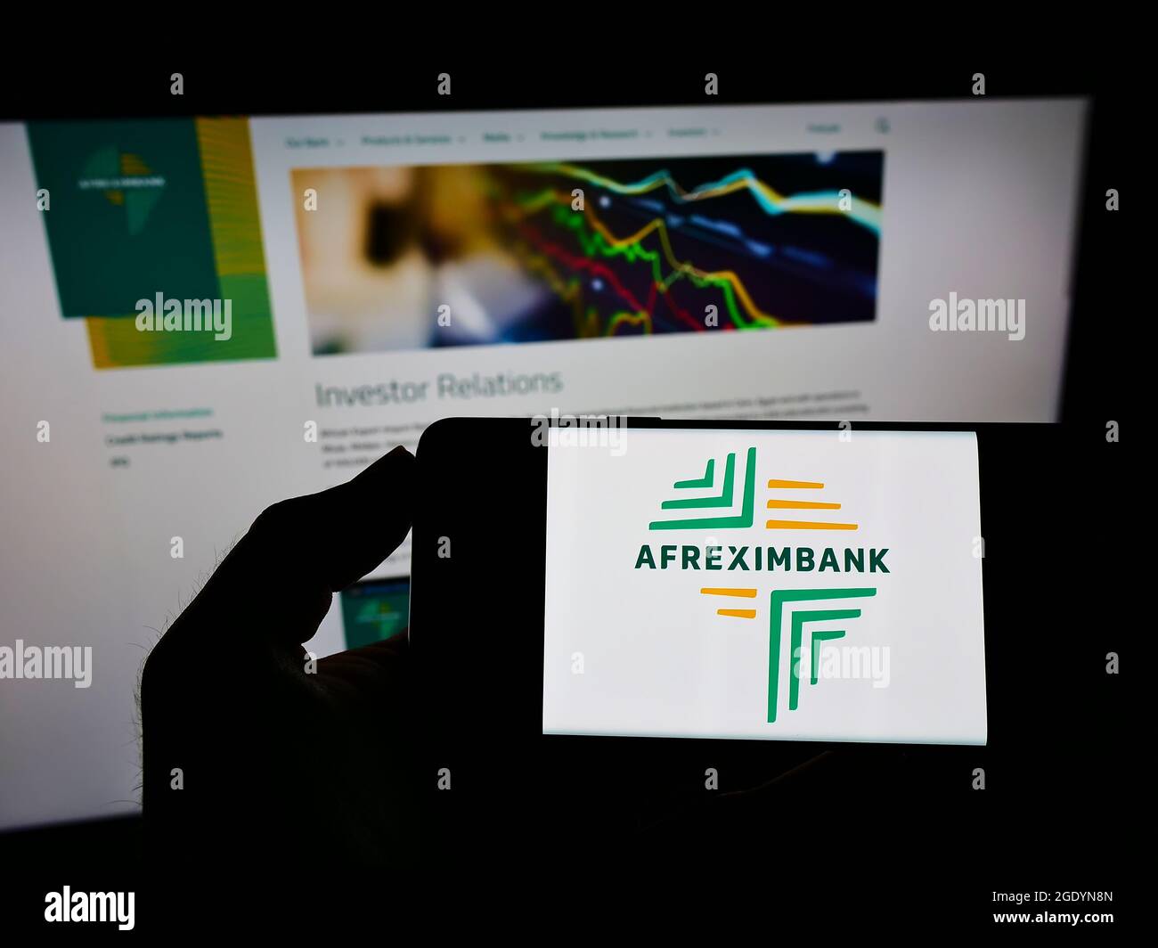 Person holding mobile phone with logo of company African Export–Import Bank (Afreximbank) on screen in front of web page. Focus on phone display. Stock Photo