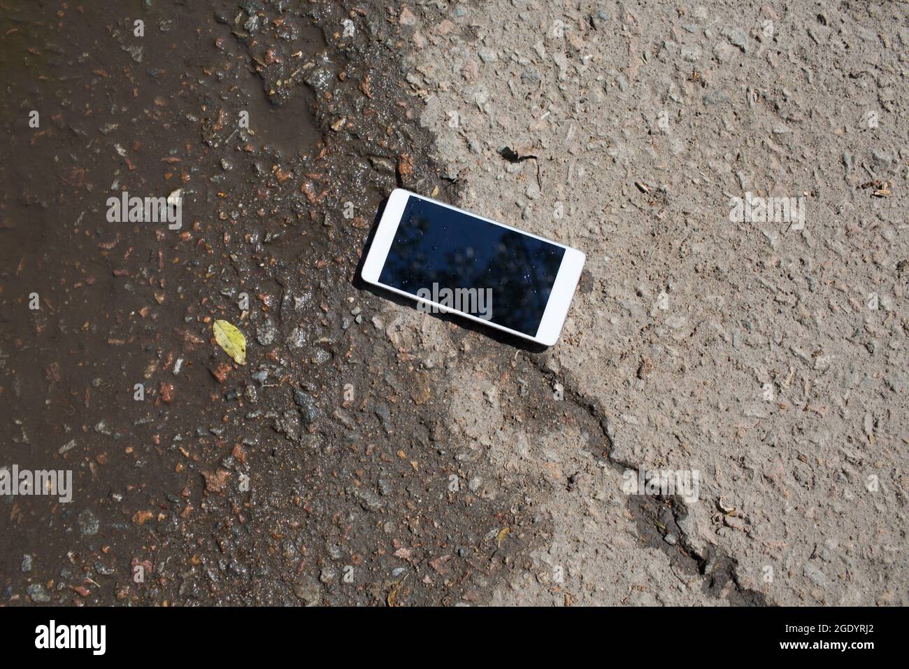 Mobile phone lying on pavement in puddle Stock Photo