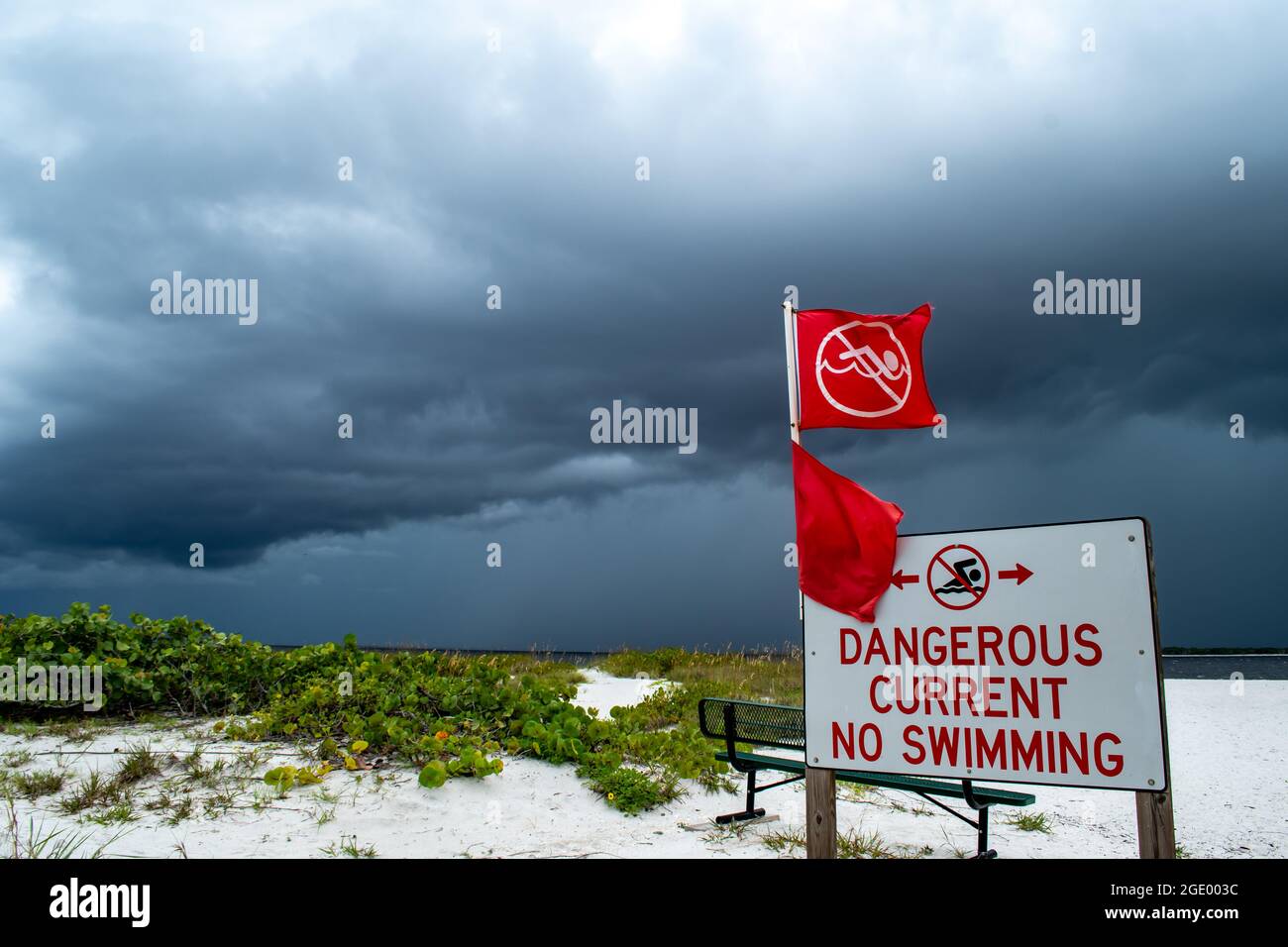Warning signs on the beach with red flags; Port Boca Grande Lighthouse and Museum, Gasparilla Island as a tropical storm with black clouds gather Stock Photo