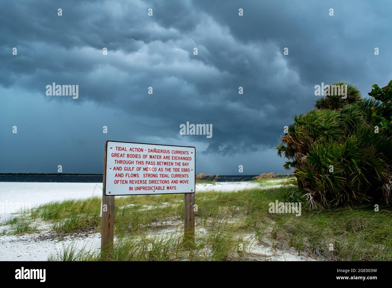 Warning signs on the beach with red flags; Port Boca Grande Lighthouse and Museum, Gasparilla Island as a tropical storm with black clouds gather Stock Photo