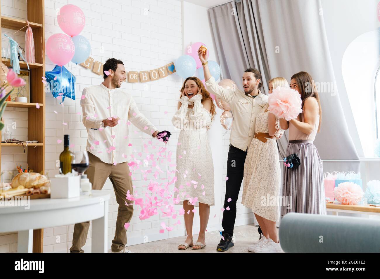 Young excited couple blowing up surprise balloon during gender reveal party indoors Stock Photo