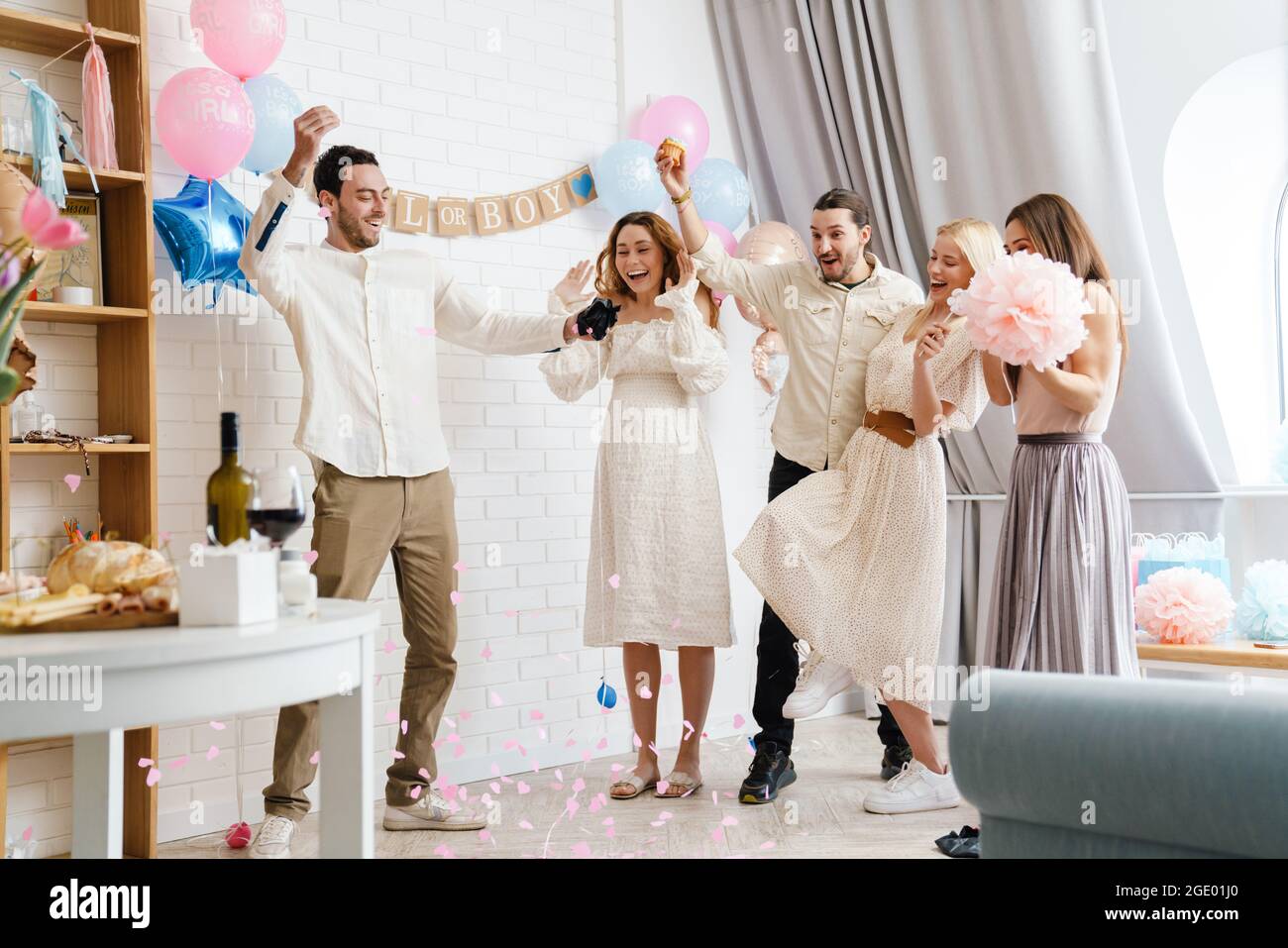 Young excited couple blowing up surprise balloon during gender reveal party indoors Stock Photo