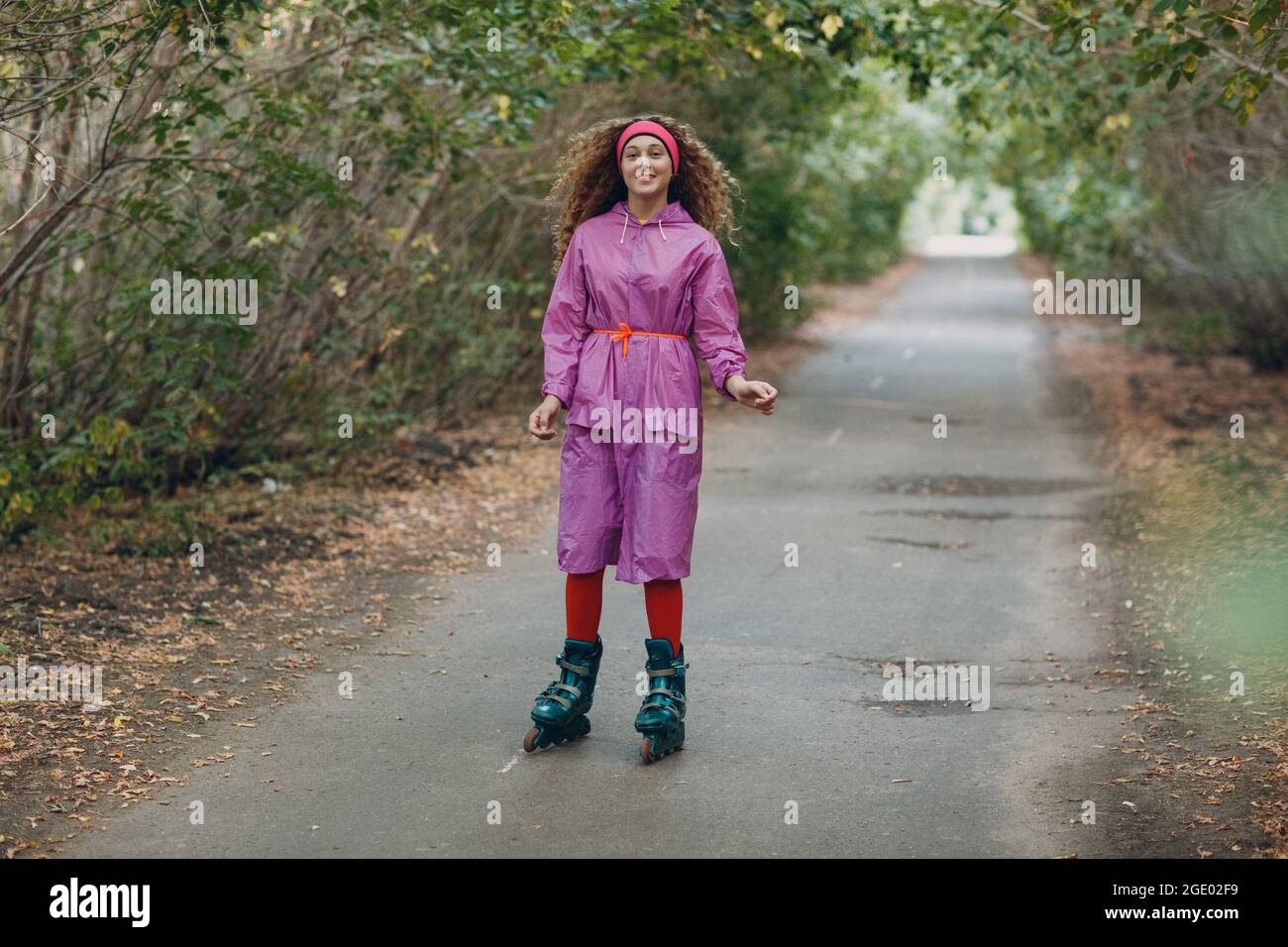 Foto de Enjoying herself. Pretty curly girl enjoying roller-skating down  the street and spreading her hands wide while smiling do Stock