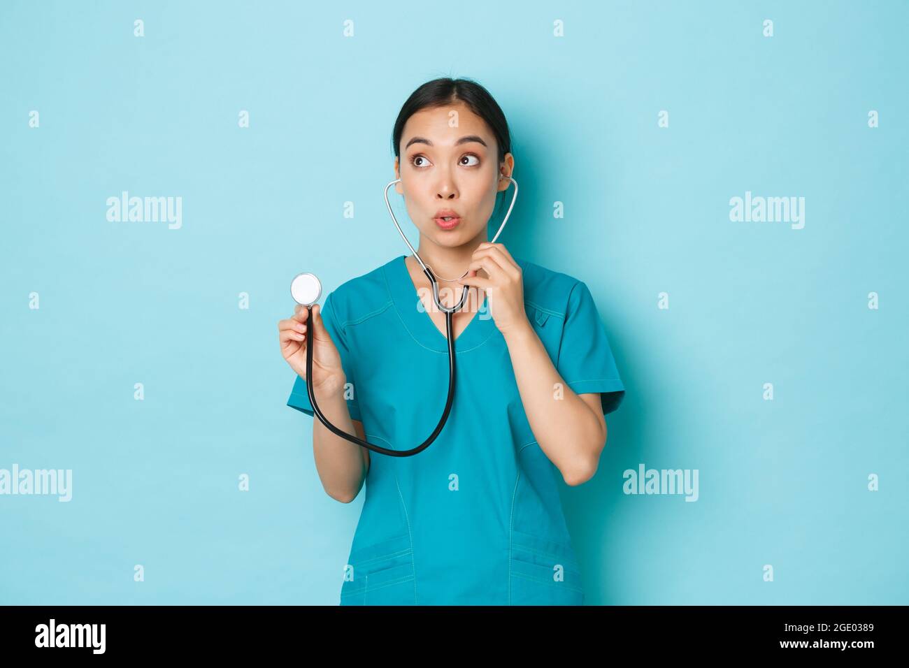 Covid-19, social distancing and coronavirus pandemic concept. Surprised asian female doctor, nurse listening to patient lungs with stethoscope and Stock Photo