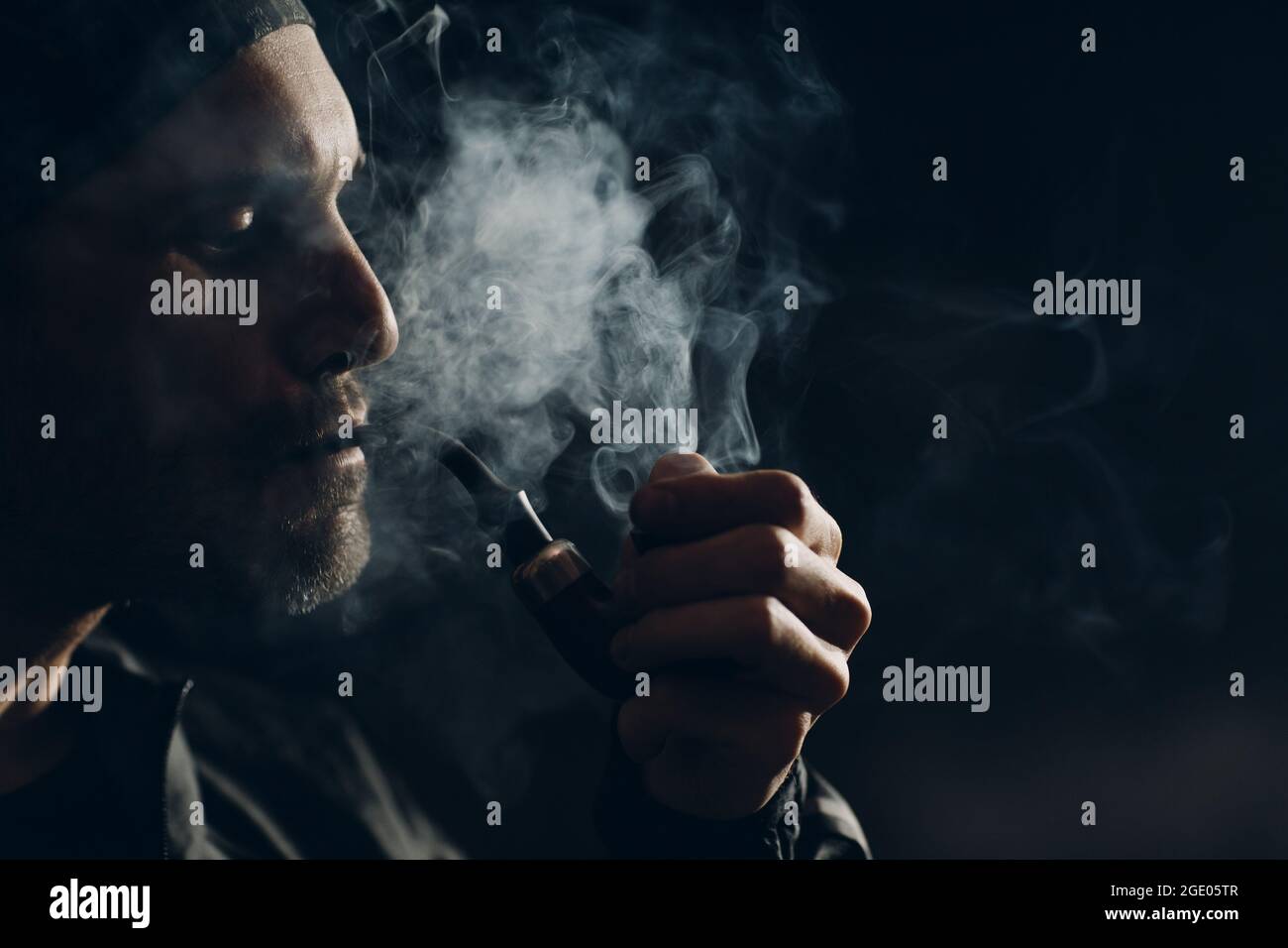 Man Smokes Smoking Pipe Against Dark Background Back Side Lit Profile