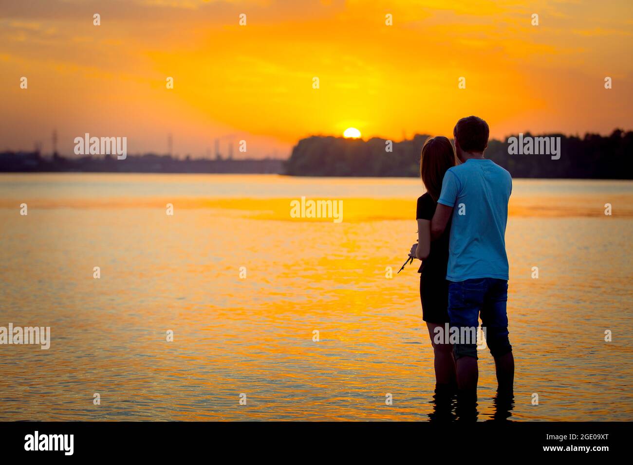 Silhouette of a couple enjoying the sunset sky over the river at dusk ...
