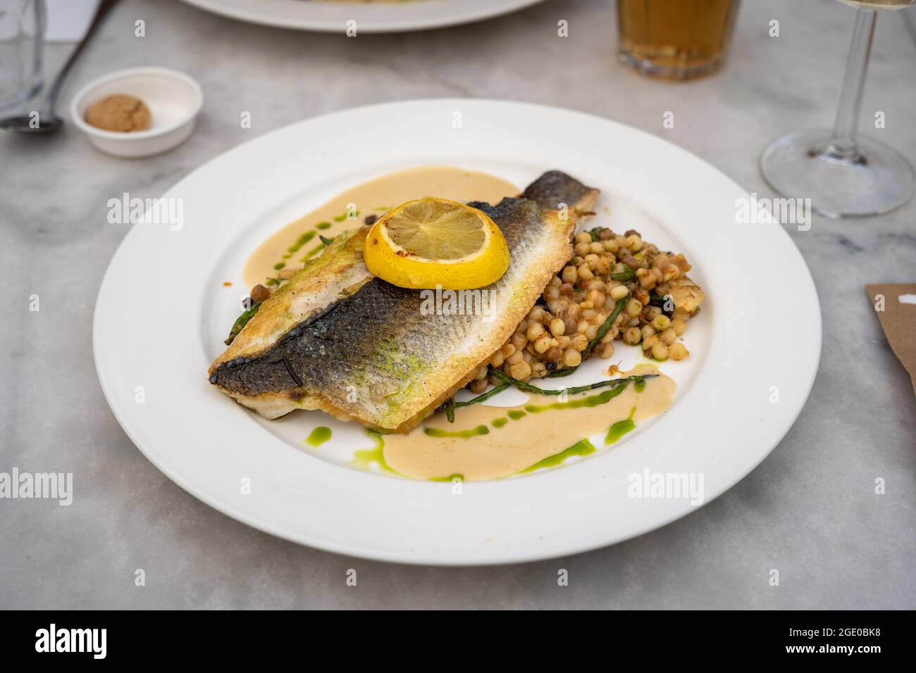A plate with a piece of fish with lemon and pearl couscous, eating out at a restaurant Stock Photo