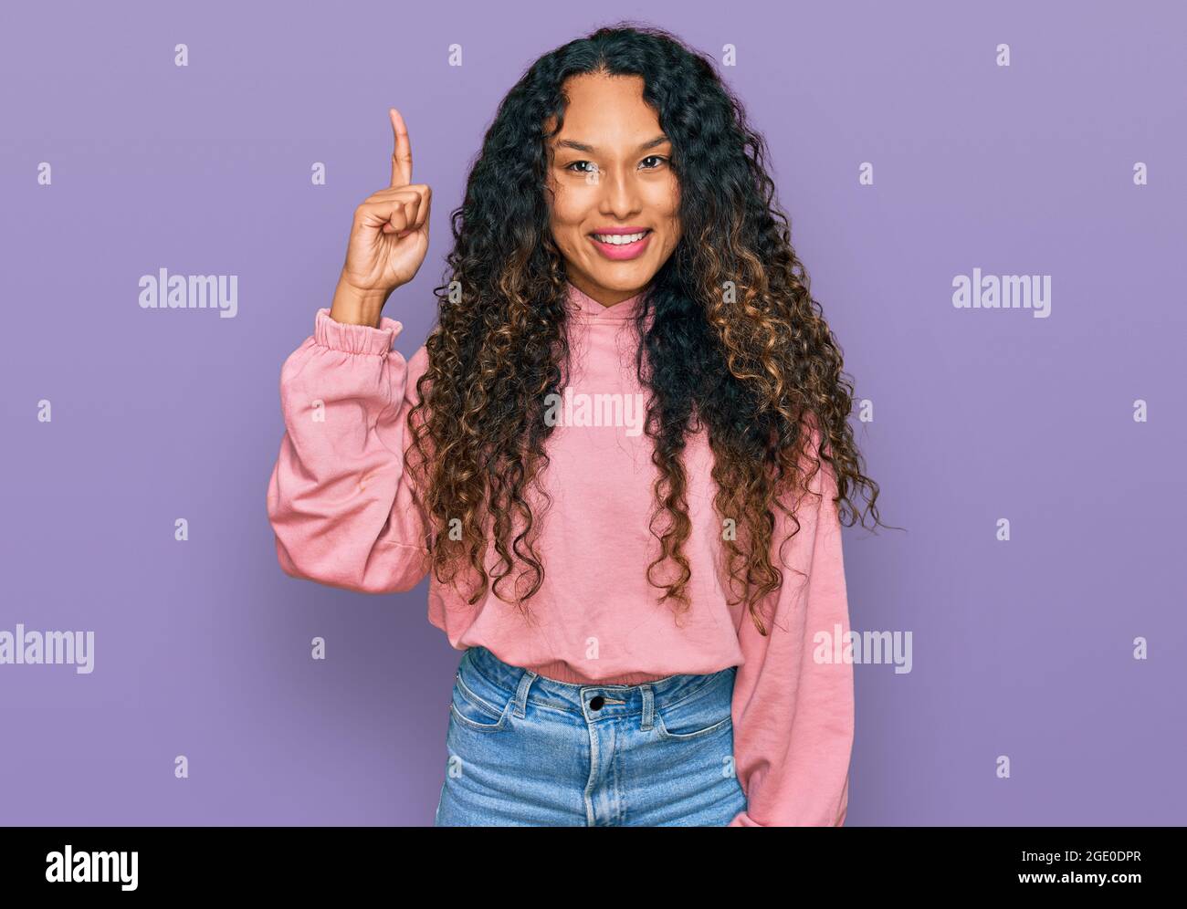 Young hispanic woman with curly hair wearing casual sweatshirt pointing