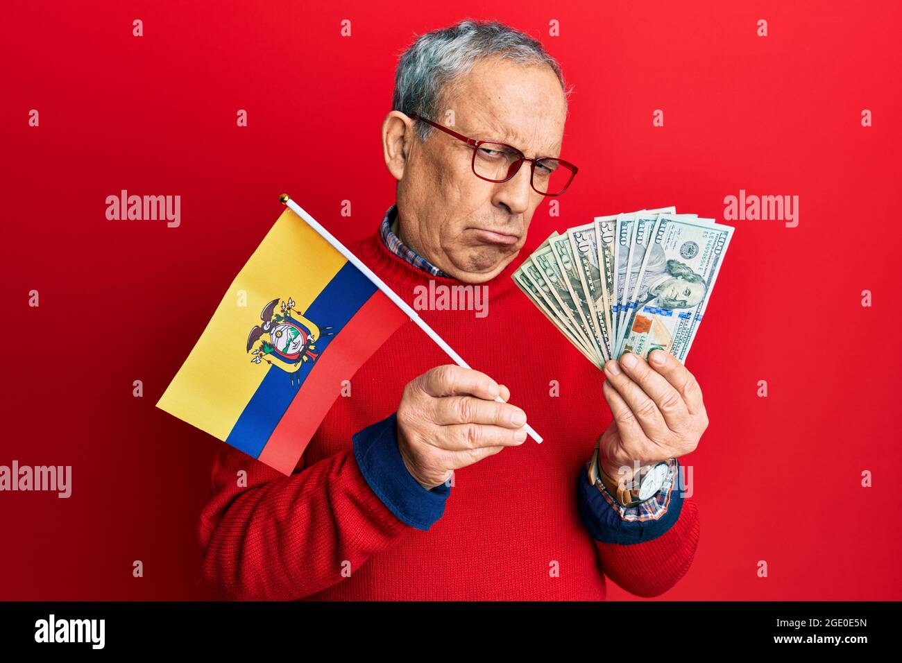 Handsome senior man with grey hair holding ecuador flag and dollars depressed and worry for distress, crying angry and afraid. sad expression. Stock Photo