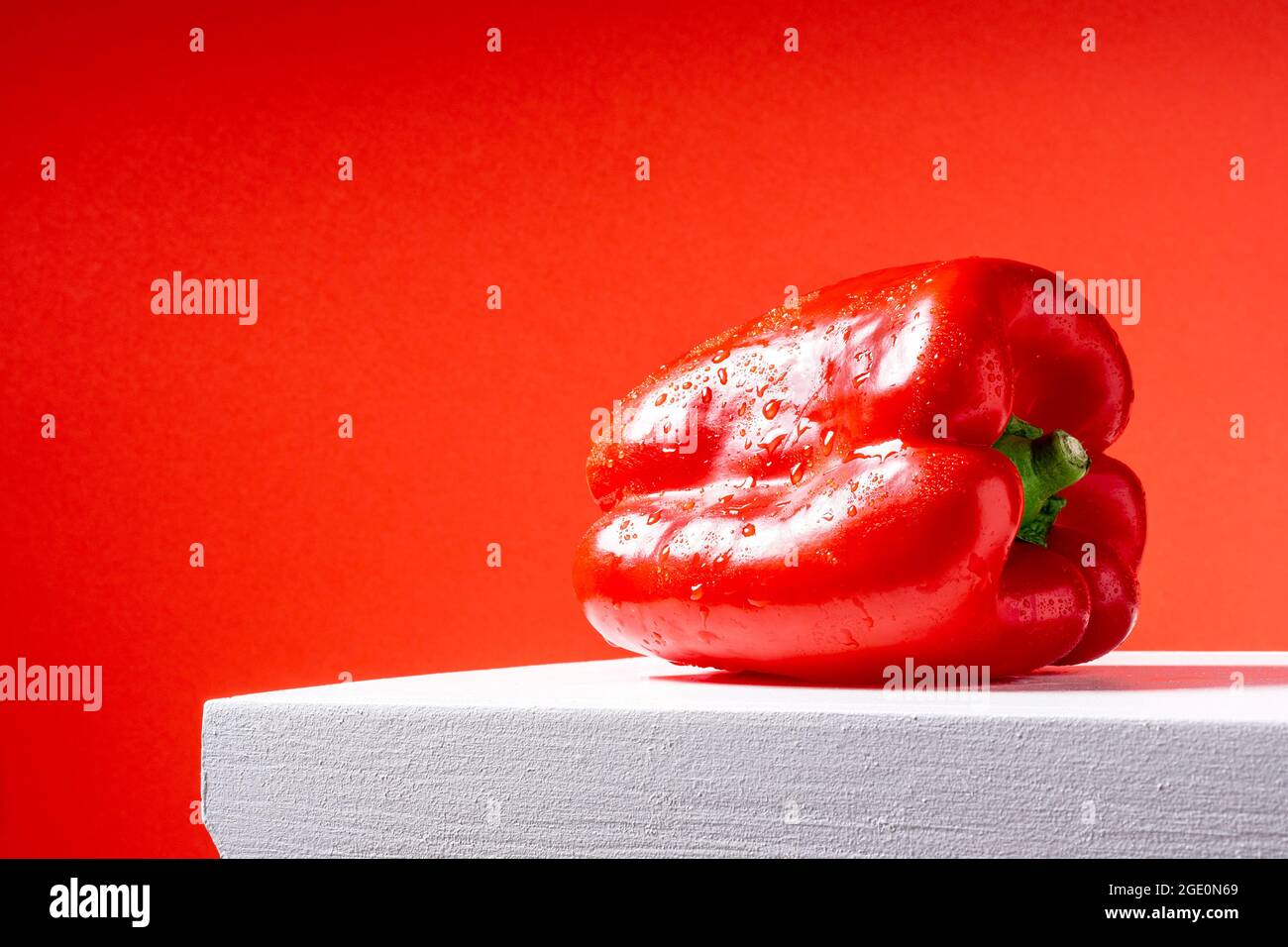 Photo of a wet red pepper on a white table and red background.The photograph is taken in horizontal format and has space to put text. Stock Photo