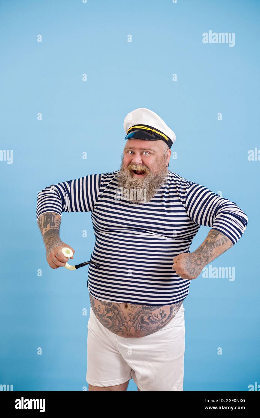 Dashing plus size person wearing sailor costume with pipe poses on light blue background Stock Photo