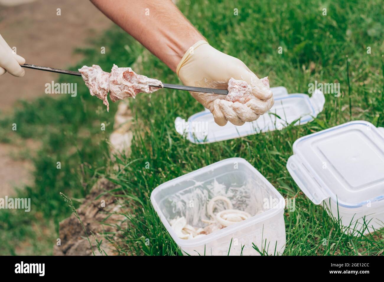 Male hands in white gloves stringing raw meat in marinade on skewers