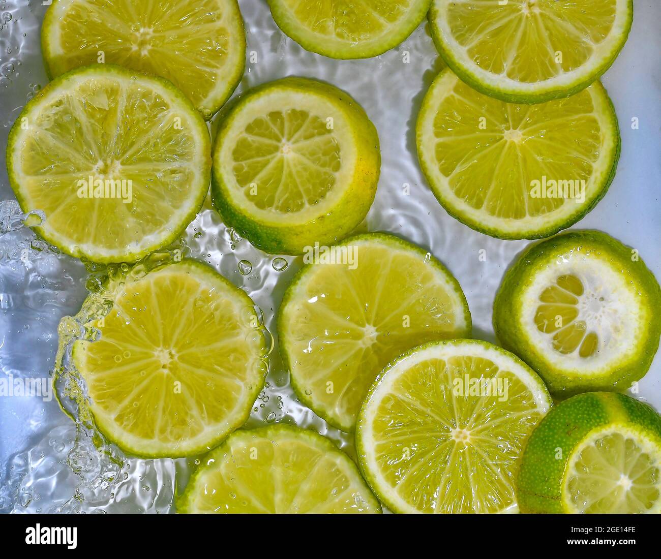 Limes close-up in liquid with bubbles. Slices of green ripe limes in water. Close-up fresh slices of yellow limes on white background Stock Photo