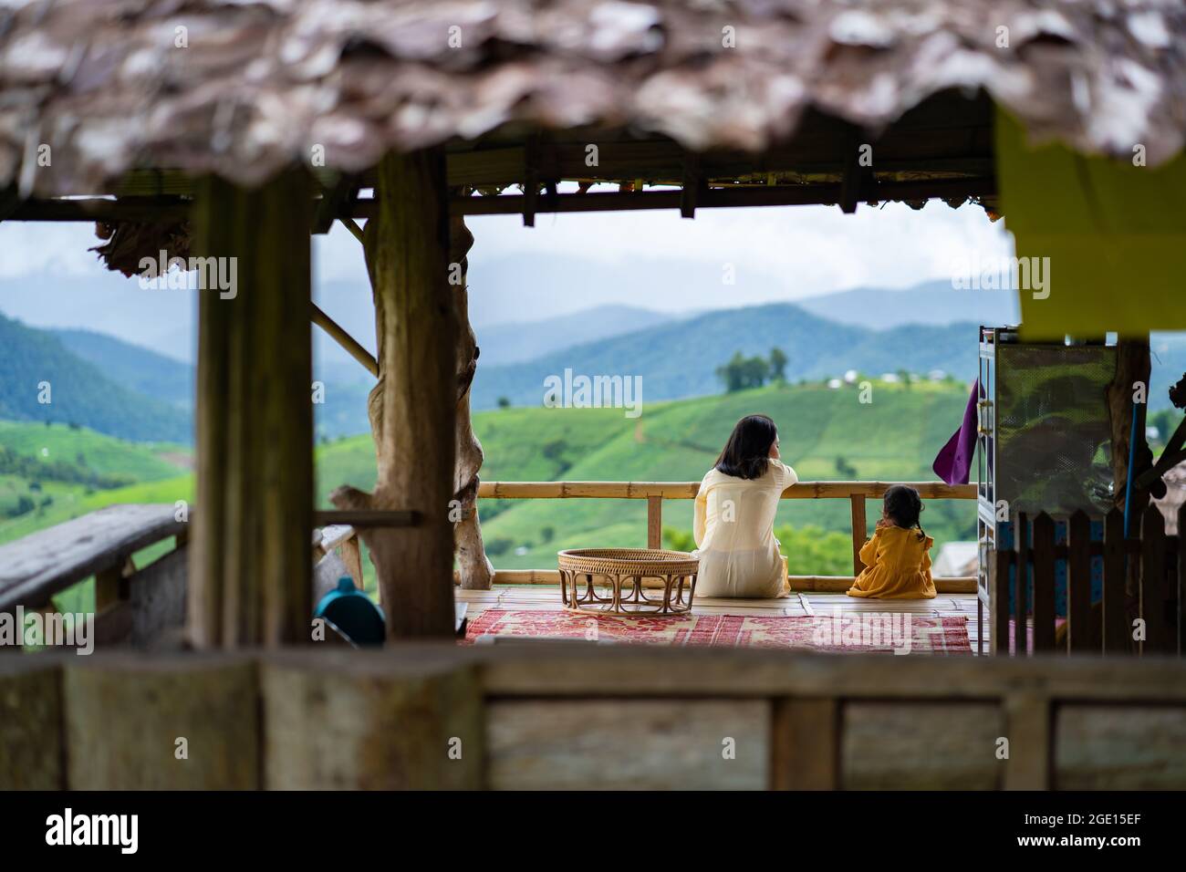 A rear view of mother and daughter sitting at wooden cottage looking at mountainscape Stock Photo
