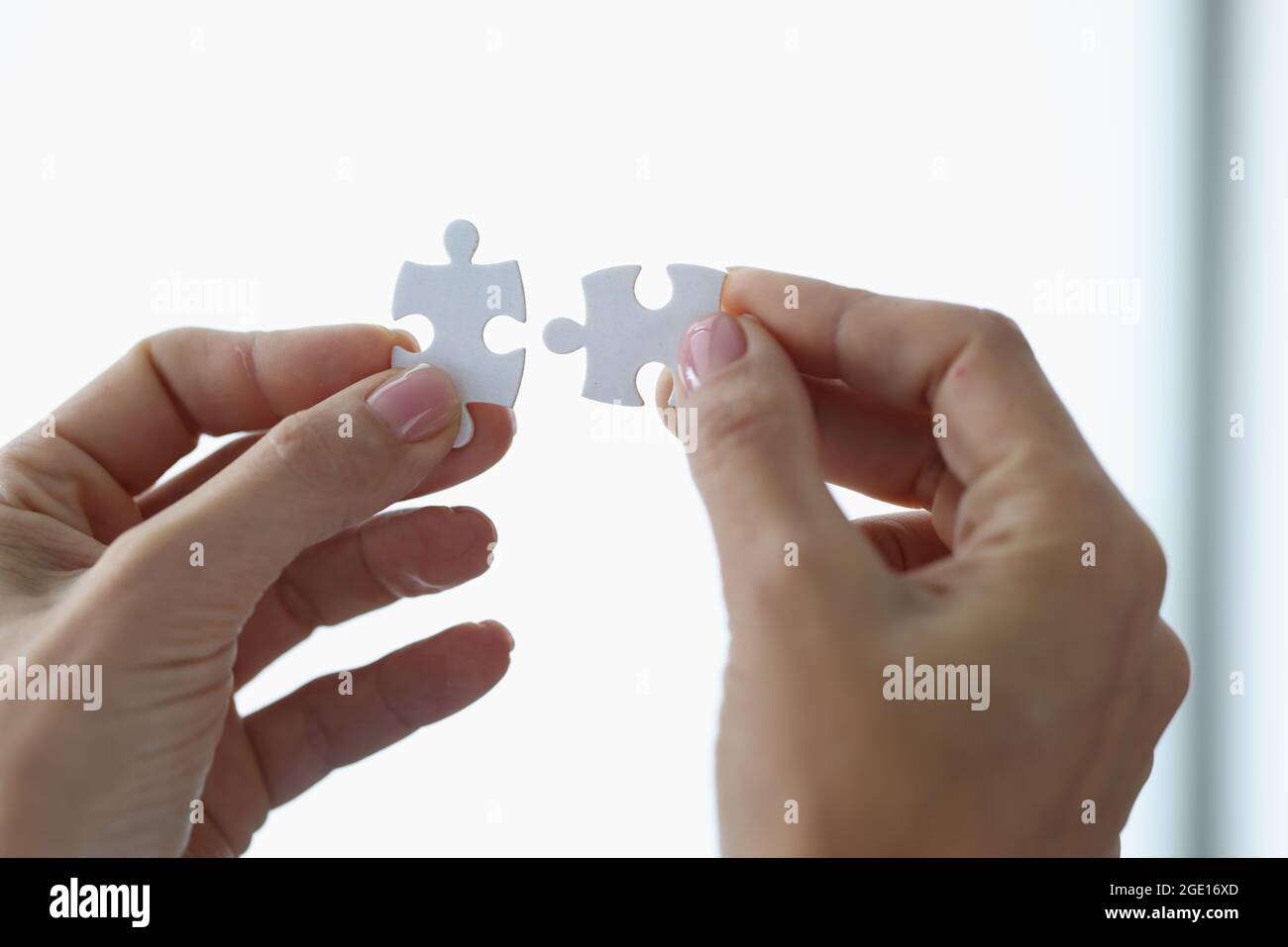 Female hands holding two white puzzle pieces closeup Stock Photo