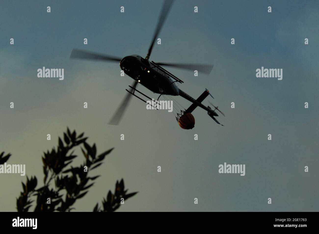 San Diego Sheriff's Bell Jet Ranger overhead with a bambi bucket during Cocos fire Stock Photo