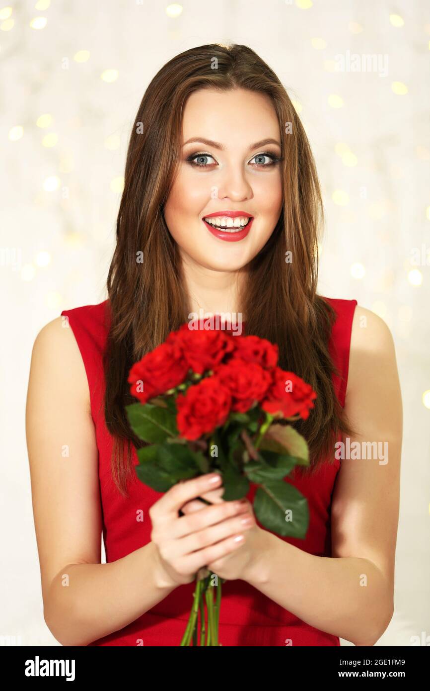 Smiling girl with bouquet of red roses on lights background Stock Photo ...