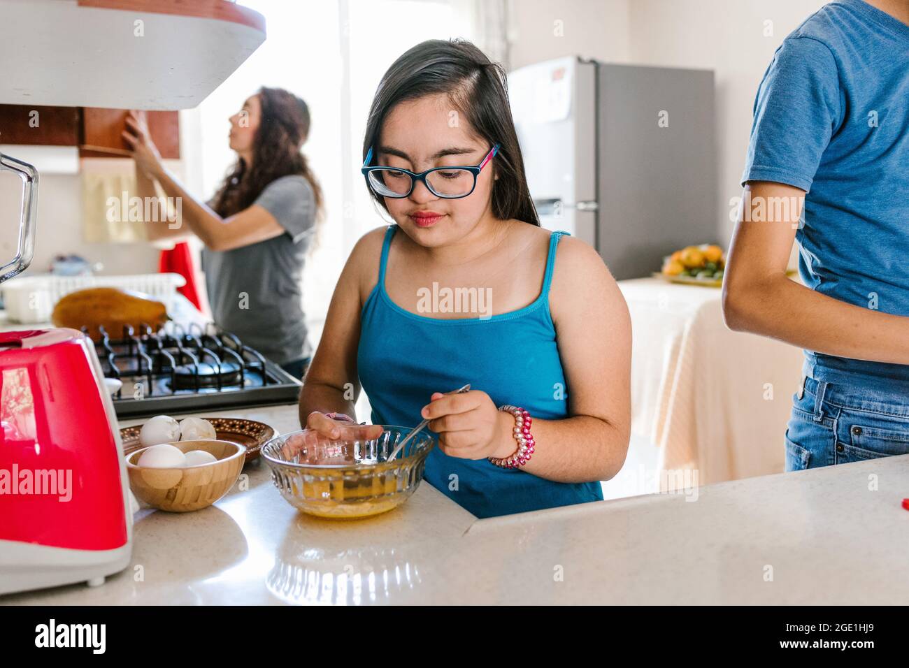 Mexican teenage girl with down syndrome with her family cooking in the kitchen at home, in disability concept in Latin America Stock Photo