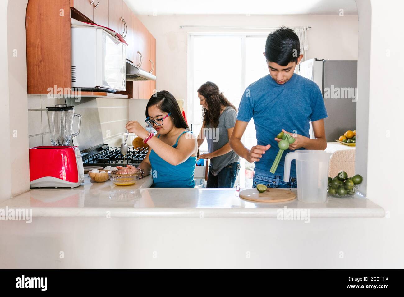 Mexican teenage girl with down syndrome with her family cooking in the kitchen at home, in disability concept in Latin America Stock Photo