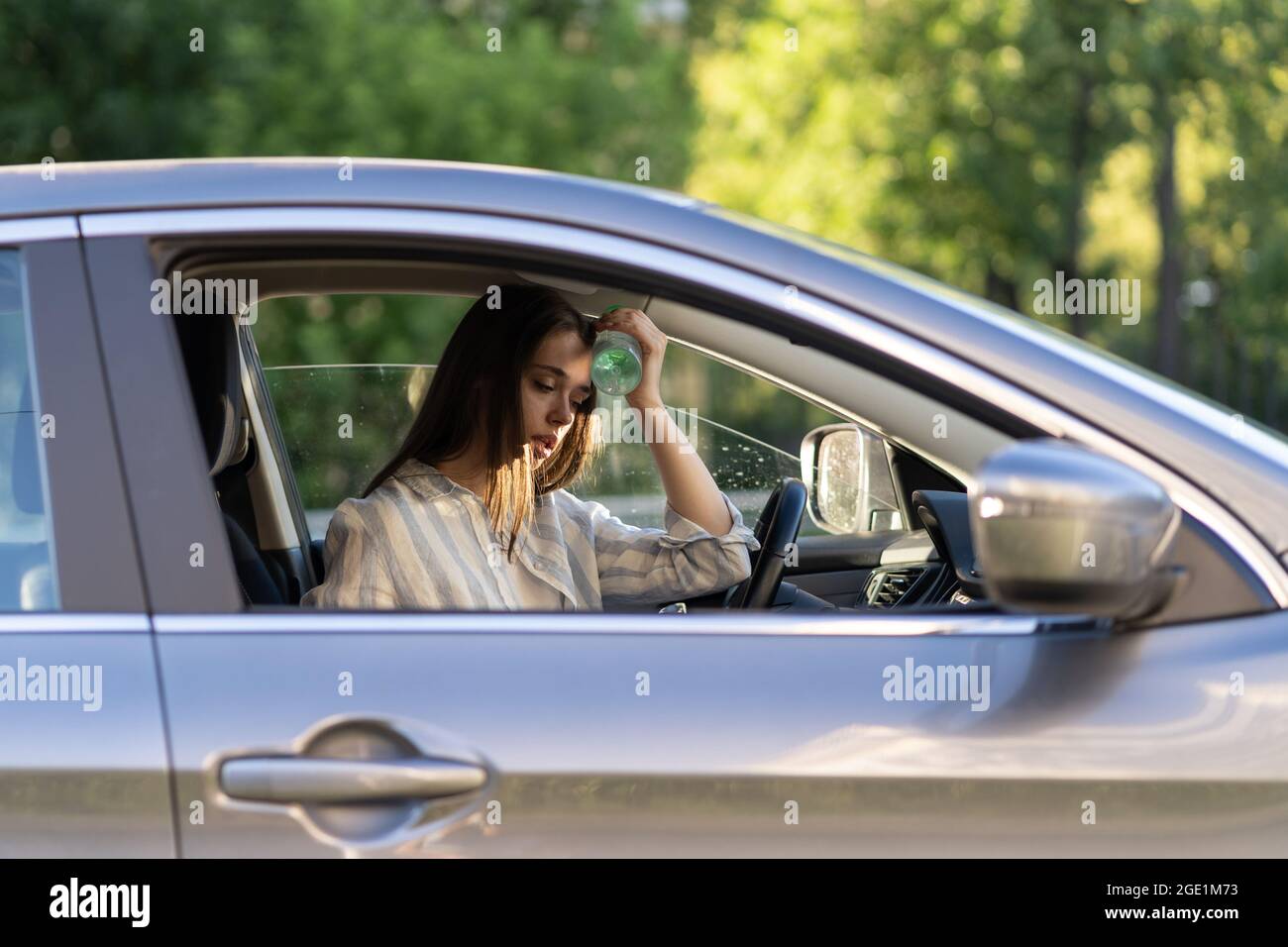 Exhausted girl driver suffering from headache, heat, hot weather applies bottle of water to forehead Stock Photo