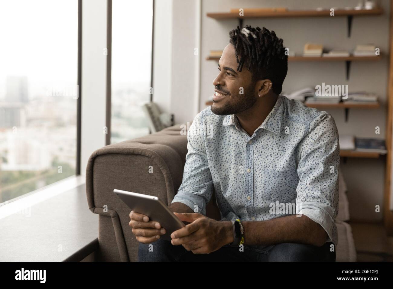 Smiling African guy holding digital tablet looking out window Stock Photo