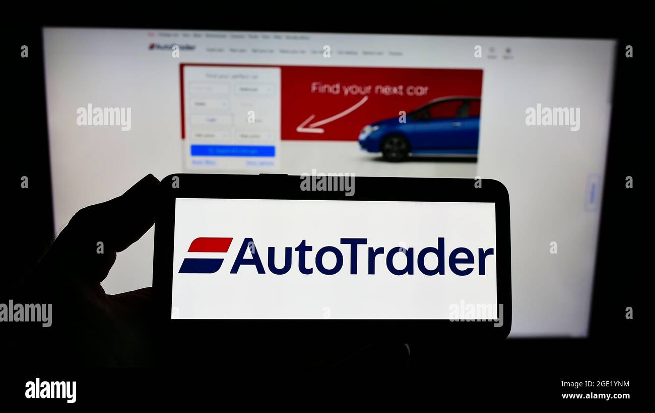 Person holding smartphone with logo of US online car marketplace Autotrader.com Inc. on screen in front of website. Focus on phone display. Stock Photo