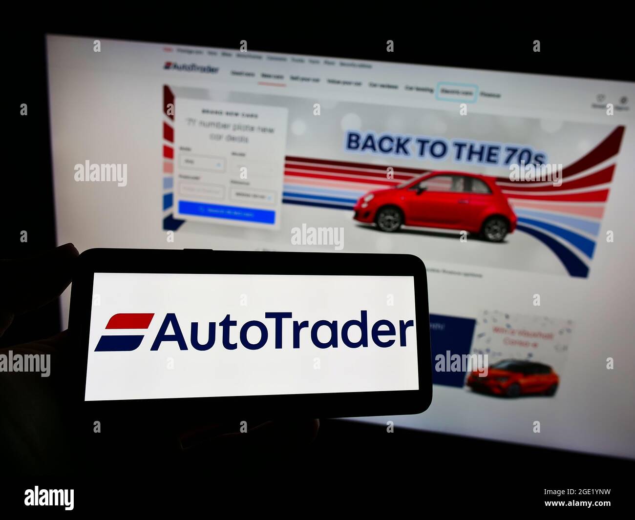 Person holding mobile phone with logo of American online car marketplace Autotrader.com Inc. on screen in front of web page. Focus on phone display. Stock Photo