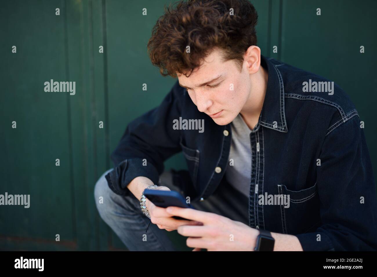 Portrait of young man against green background outdoors, using smartphone. Stock Photo
