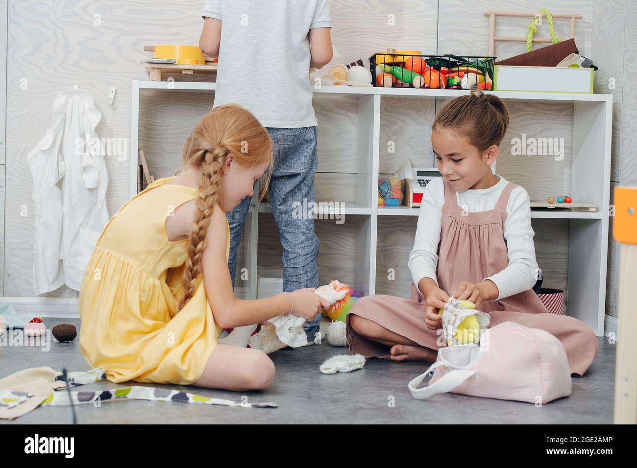 Joyful little girls playing with dolls trying on different clothes. Stock Photo