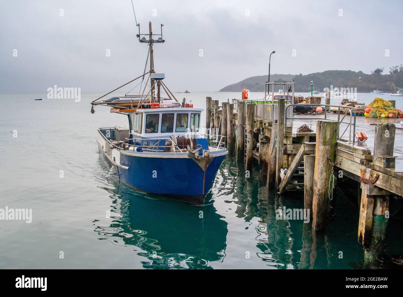 A fishing boat docked at the wharf, floats on the still sea, waiting for the next trip out on the ocean Stock Photo