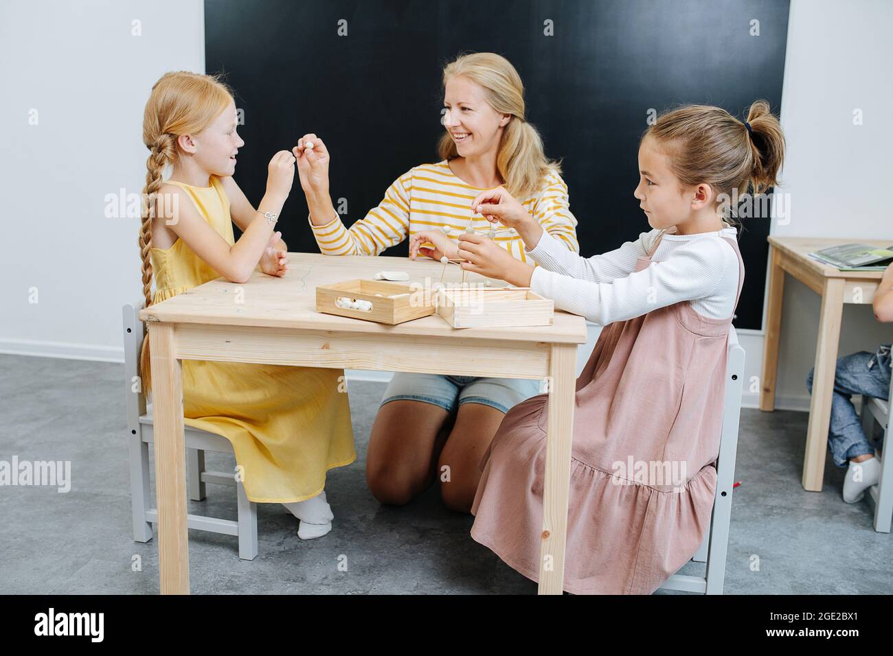 Smiling teacher helping girls to build 3d shapes from plasticine and toothpicks Stock Photo