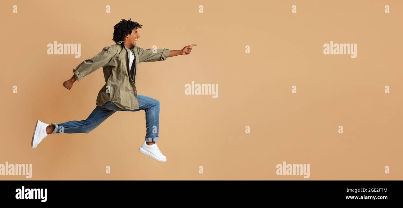 Look There. Overjoyed black guy pointing aside while jumping up in air Stock Photo