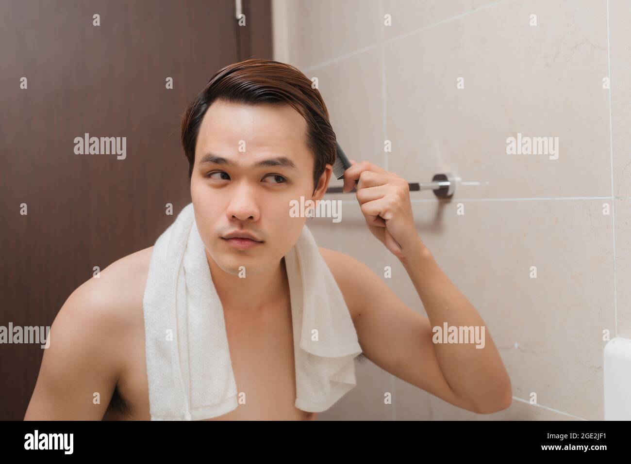 Morning routine. Rear view of handsome young man combing his hair while standing against a mirror Stock Photo