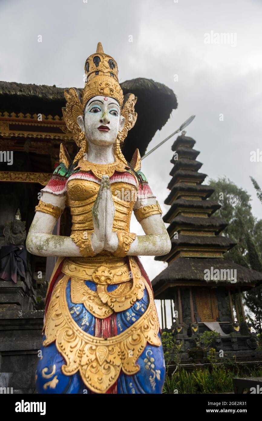 Colorful statue of a female goddess in the Ulun Danu Batur temple. Meru tower in the background. Bali, Indonesia. Stock Photo