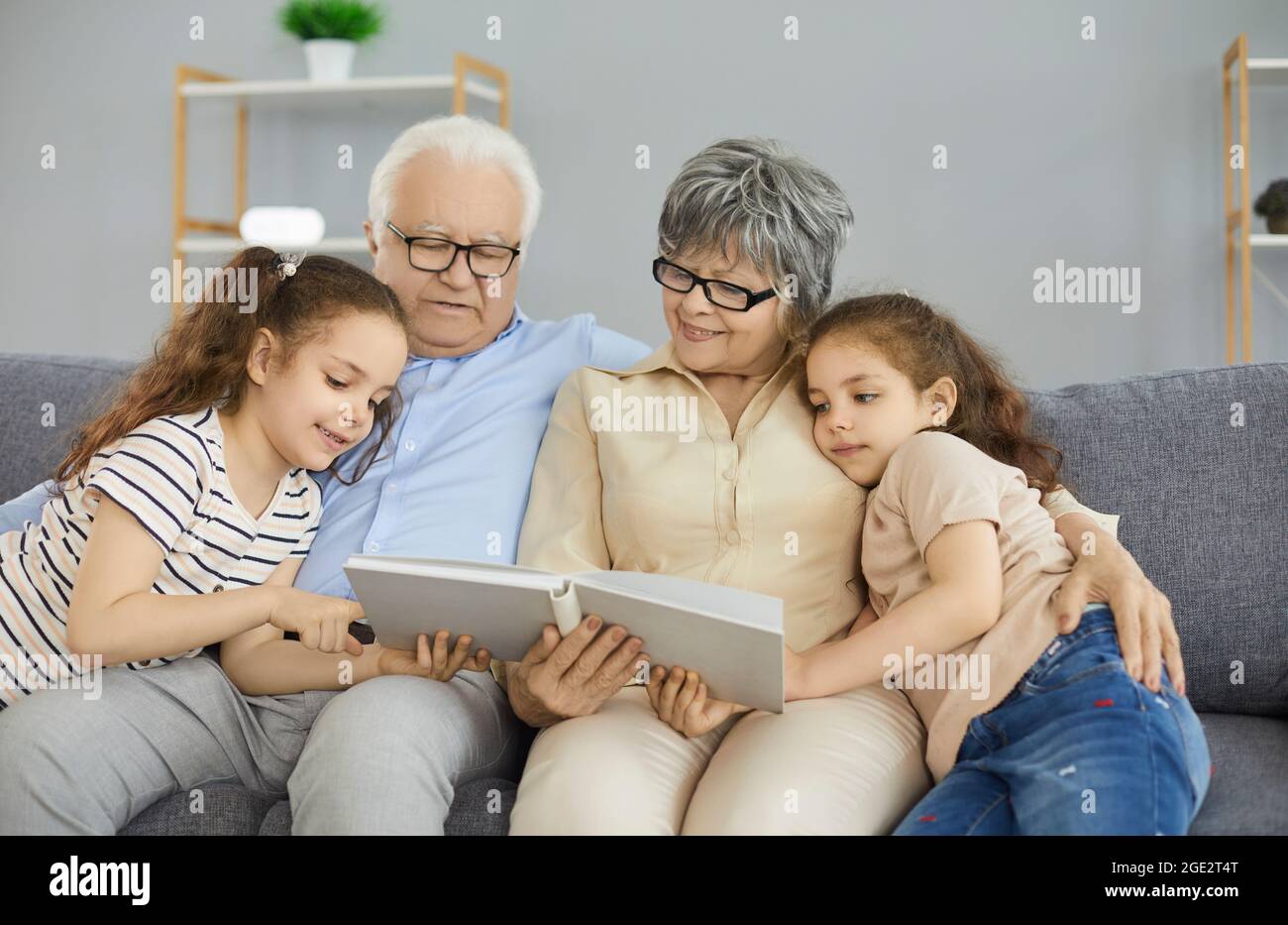 Happy grandma, grandpa and grandkids reading a book or looking through a family photo album Stock Photo