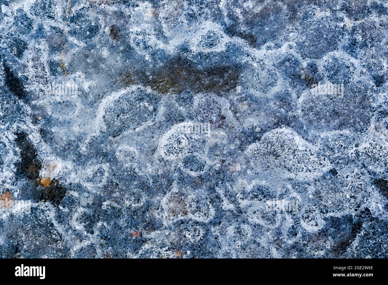 Ice encapsulating small stones, leaves and air bubbles, creating a highly textured effect Stock Photo