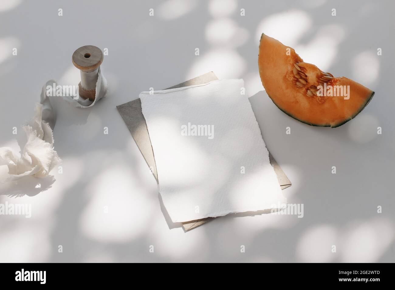 Summer food still life composition. Cantaloupe melon fruit, silk ribbon. White table background with tree shadows overlay. Stationery mock up scene Stock Photo